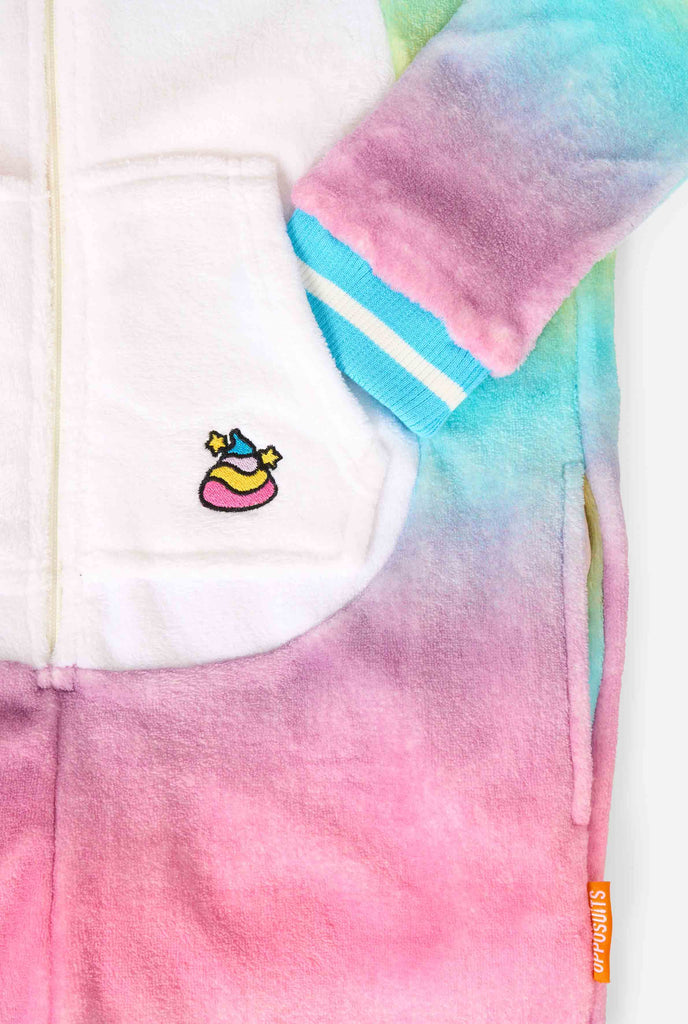 A smiling kid is wearing a white, pink, blue and yellow kids onesie designed as a unicorn. The Unicorn onesie features a hood resembling a unicorn head and other playfull details. Close-up pocket.