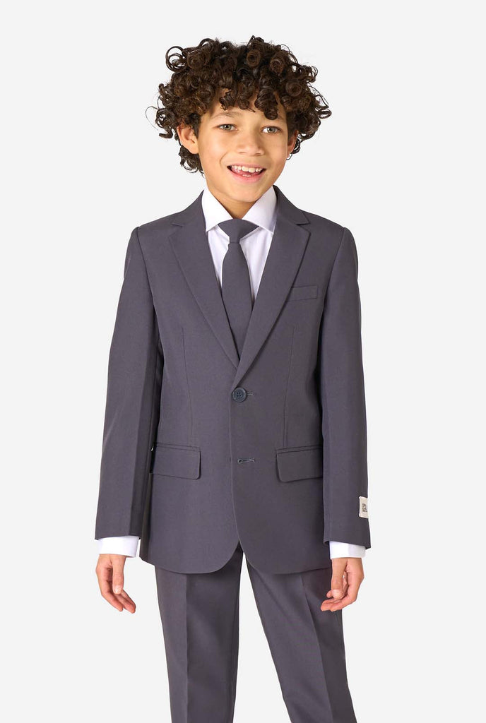 Kid wearing a stylish charcoal colored grey suit with a white dress shirt, smiling confidently. Perfect formal outfit for boys' special occasions, weddings, and parties.