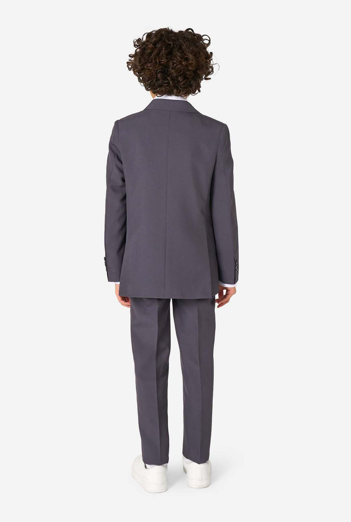 Kid wearing a stylish charcoal colored grey suit with a white dress shirt, smiling confidently. Perfect formal outfit for boys' special occasions, weddings, and parties. View from the back.