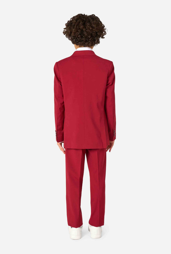 Kid wearing a stylish burgundy red suit with a white dress shirt, looking confidently. Perfect formal outfit for boys' special occasions, weddings, and parties. View from the back.